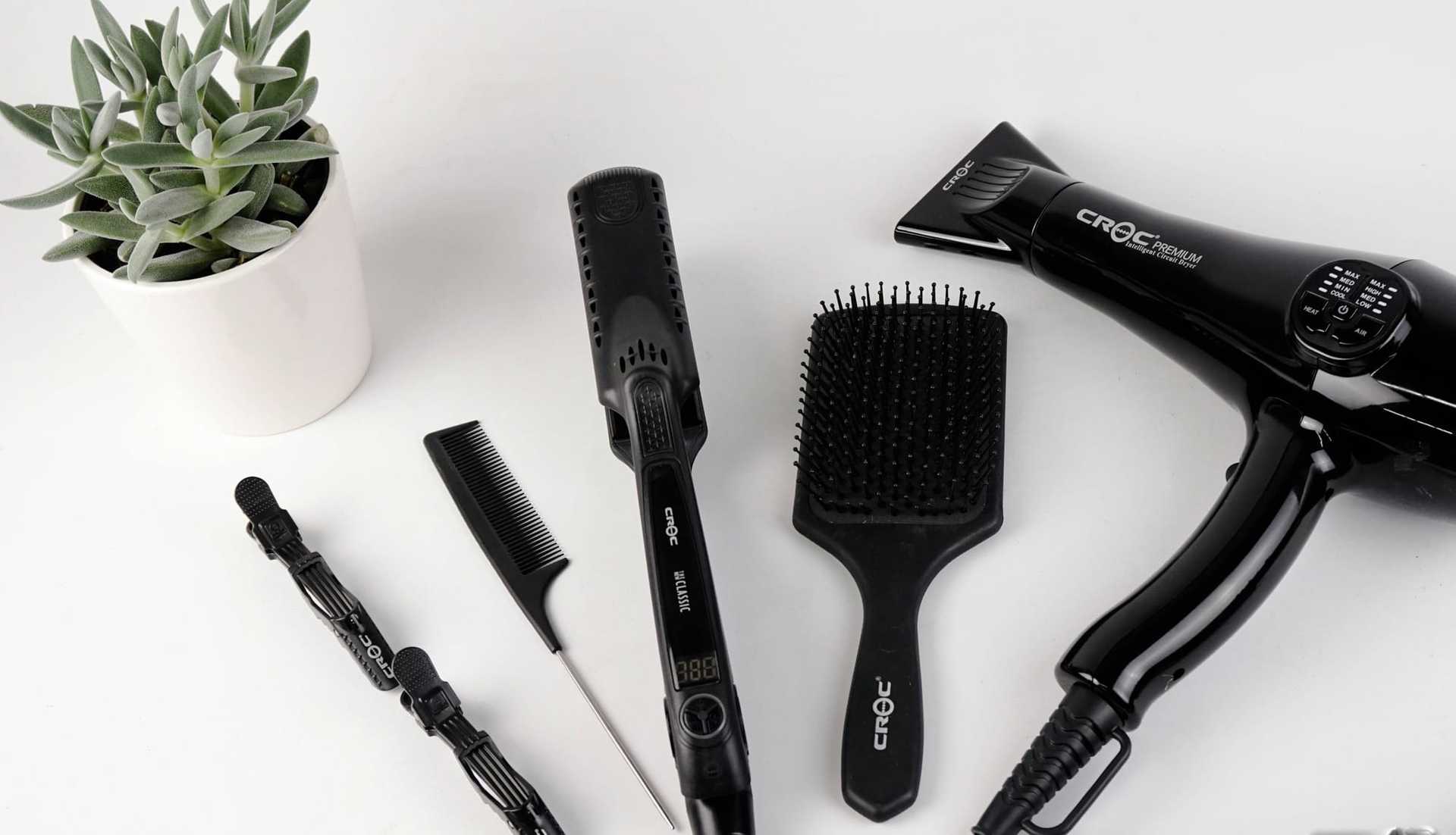 Hair styling tools: straighteners, brush, clips, comb, and hairdryer near a plant.